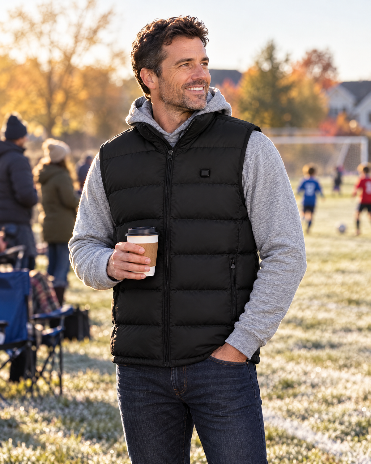 Man wearing the black heated vest over a hoodie on the sidelines of a soccer game