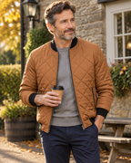 Man wearing the tan diamond quilted bomber jacket over a grey jumper outside a country pub